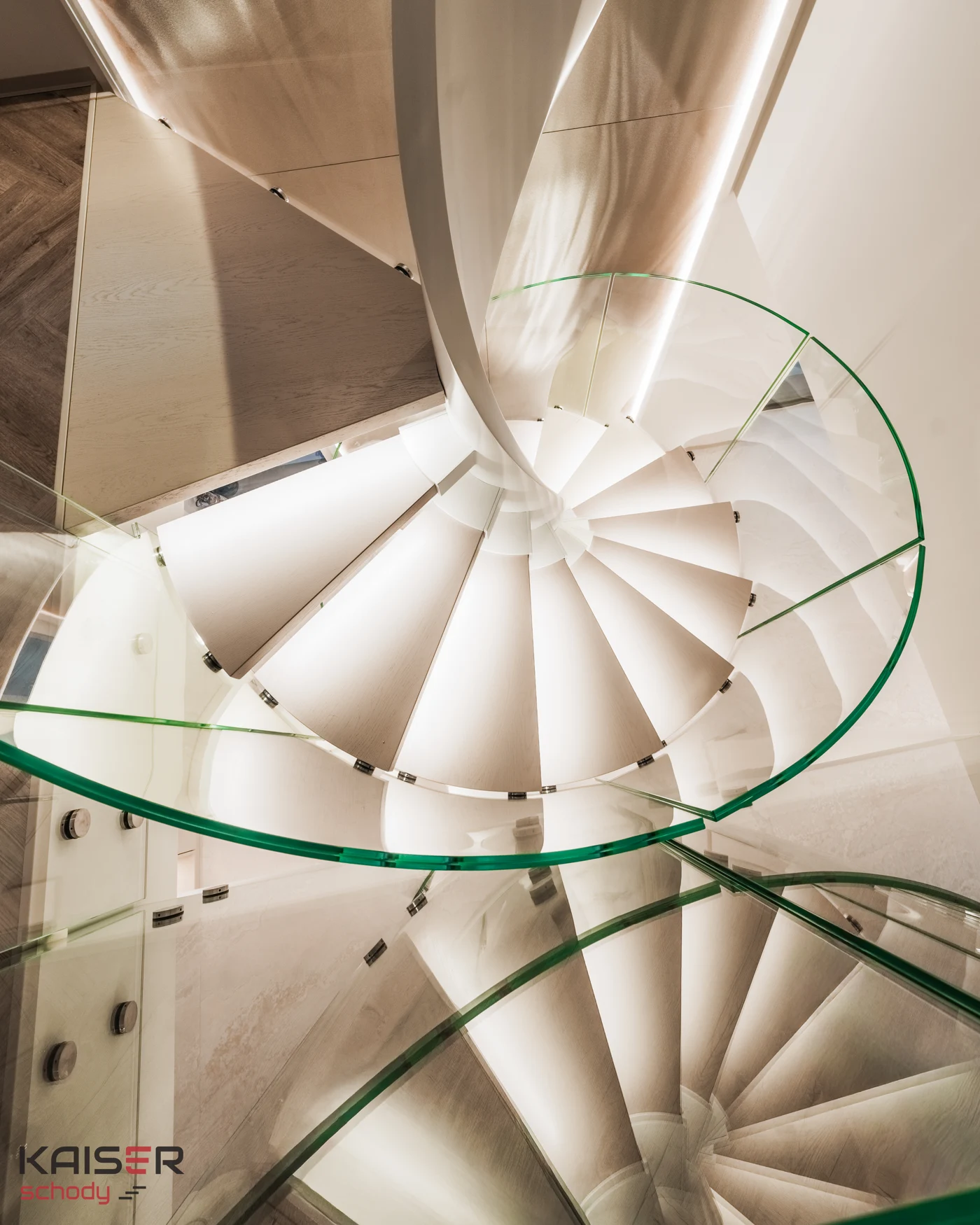 Light-coloured spiral staircase and curved glass balustrade viewed from above
